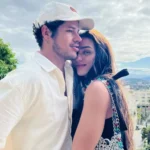 José Loreto, usando boné e camisa branca, abraça carinhosamente Rafa Kalimann, que veste blusa escura com detalhes coloridos. O casal está ao ar livre, com paisagem urbana ao fundo. Imagem representa o relacionamento de José Loreto e Rafa Kalimann.
